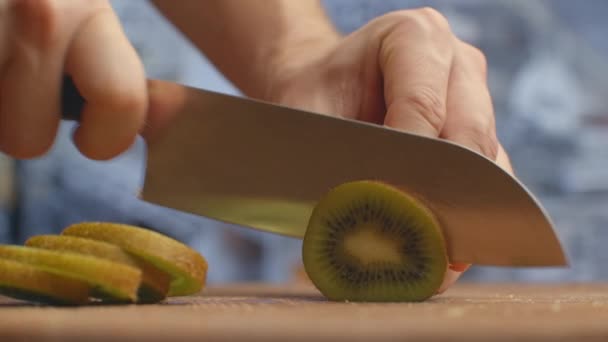 Cortar con un cuchillo en una tabla de madera kiwi primer plano en la cocina. triturar . — Vídeos de Stock