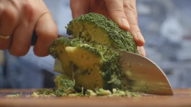 Cortar con un cuchillo en una tabla de madera brócoli primer plano en la cocina. triturar . — Vídeo de stock