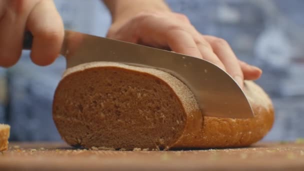 Pão cortado com uma faca em uma tábua de madeira closeup na cozinha. trituração . — Vídeo de Stock