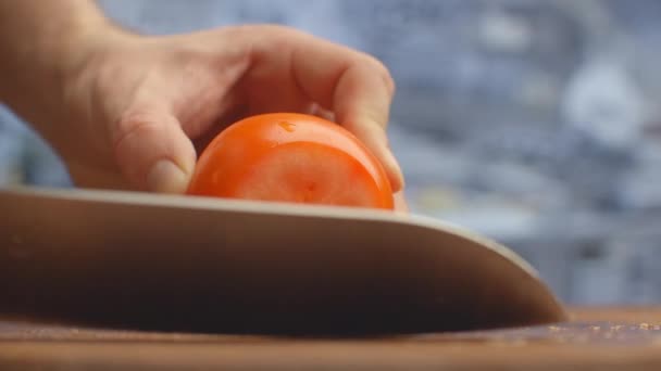 Gros plan d'une femme coupant et coupant la tomate au couteau sur une planche de bois . — Video