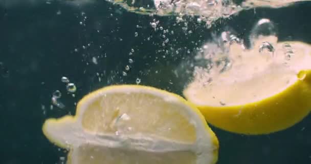 Várias frutas de limão caem dentro de um tanque de água e perturbam a água. Três frutos de limão amarelos brilhantes caem dentro de um tanque de água e retornam à superfície . — Vídeo de Stock