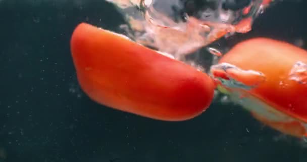 Close up several cut slices of fresh green and red bell pepper thrown and floating in clear transparent water, low angle side view, slow motion. — Stock Video