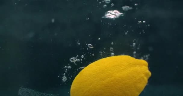 Diversi frutti di limone cadono all'interno di un serbatoio d'acqua e disturbano l'acqua. Tre frutti di limone giallo brillante cadono all'interno di un serbatoio d'acqua e tornano in superficie . — Video Stock