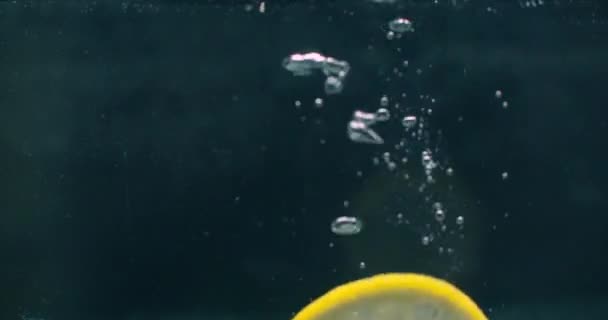 Λεμόνι που πέφτει στο νερό με φυσαλίδες σε σκούρο φόντο — Αρχείο Βίντεο