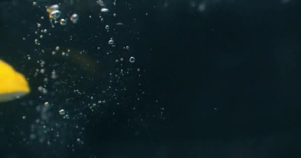 Zitrone spritzt in Superzeitlupe ins Wasser auf schwarzem Hintergrund. — Stockvideo