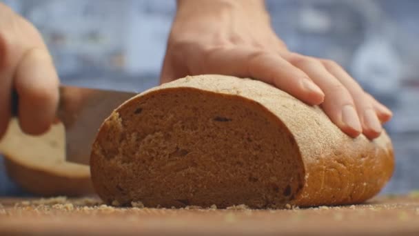 Pão cortado com uma faca em uma tábua de madeira closeup na cozinha. trituração . — Vídeo de Stock