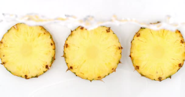 3 pineapples lie on a white in the background in slow motion falling water splashes — Stock Video