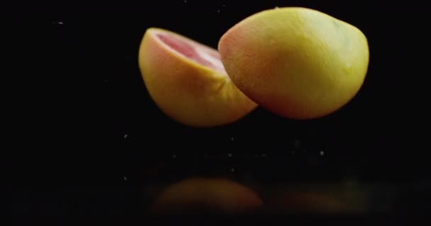 Movimento lento. toranja suculenta com baixas e quebra em 2 partes com salpicos em uma mesa de vidro com reflexão sobre um fundo escuro — Vídeo de Stock