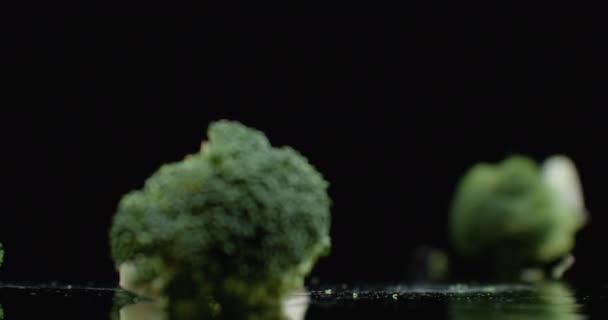 Tre broccoli verdi freschi cadono su un bicchiere con schizzi e gocce d'acqua al rallentatore. Ingredienti per insalata, cibo sano — Video Stock