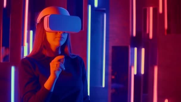 Mujer con auriculares VR pendientes rápidas de lado a lado mientras juega en el espacio oscuro iluminado luz de neón . — Vídeos de Stock