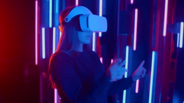 Ansiktslös kvinna bär Vr headset i mörka rymden med neon ljus lampor, användaren vänder huvudet sida vid sida ser virtuell verklighet, shoting genom färgade facklor och bokeh på förgrunden. — Stockvideo