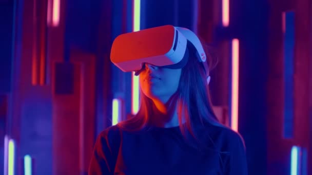 Gesichtslose Frau mit vr-Headset im dunklen Raum mit Neon-Licht-Lampen, Benutzer dreht den Kopf zur Seite suchen Virtual Reality, Shoot durch farbige Fackeln und Bokeh im Vordergrund. — Stockvideo
