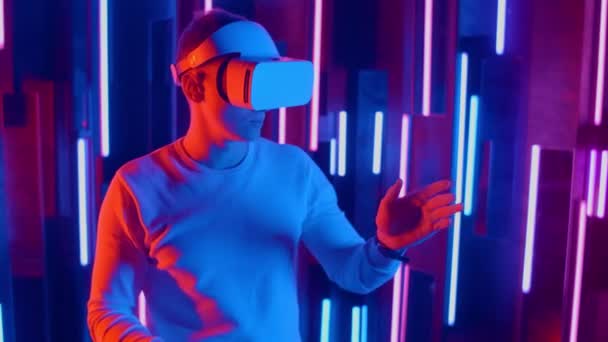 Bărbatul care poartă căști VR pante rapide dintr-o parte în alta în timp ce se joacă în spațiul întunecat iluminat lumina neonului . — Videoclip de stoc