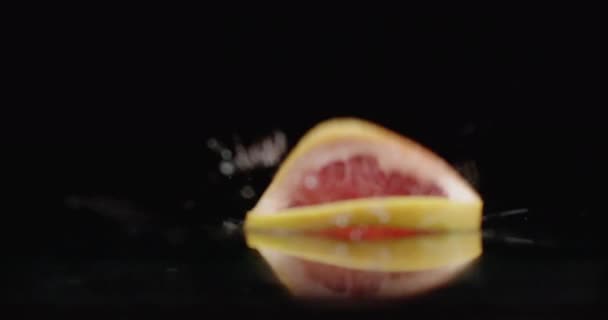 Anillos de pomelo en rodajas caen sobre el vaso con salpicaduras de agua en cámara lenta . — Vídeos de Stock