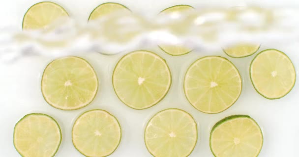 Всплески воды падают на нарезанные лимонно-зеленые кольца на белом фоне. Сверхмедленное движение — стоковое видео