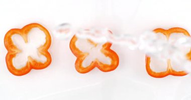 Splashes of water fall on sliced red pepper rings on a white background. Bulgarian pepper