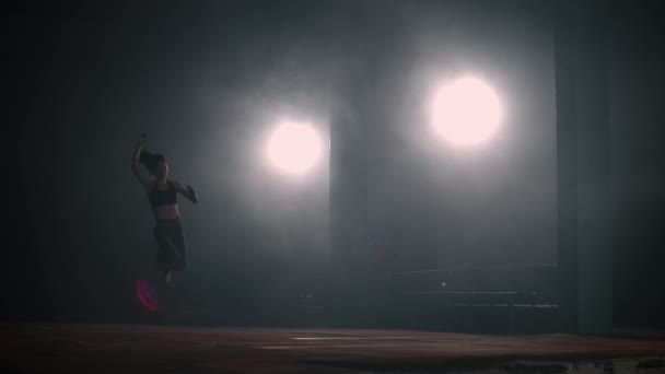 A sporty woman runs up in a stadium and performs a long jump in slow motion in a stadium on a dark background — Stok video