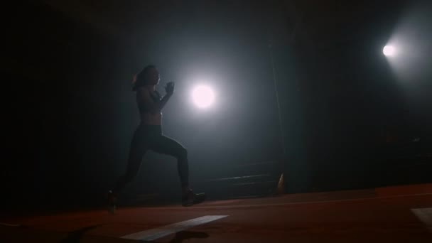 A sporty woman runs up in a stadium and performs a long jump in slow motion in a stadium on a dark background — 图库视频影像