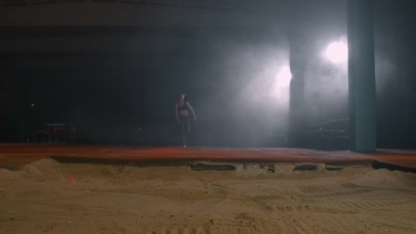 遅い動きの女性のトラックとフィールドは、実行中のスタートで長いジャンプを実行します。コンテストで砂の中に飛び込む — ストック動画