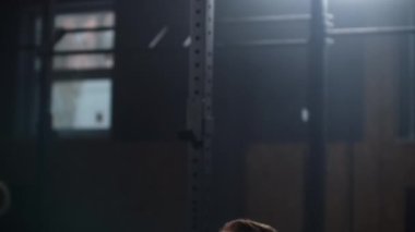 Slow motion: Young athletic man squats with barbell in gym. Man testing hes strength by holding a barbell with heavy weights on her shoulders as he squats.