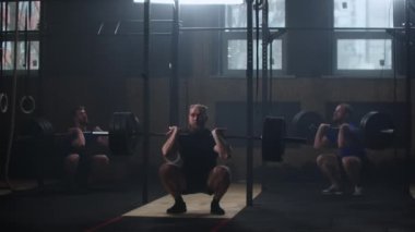 Three fitness man bodybuilder training using barbell weightlifting exercise muscular sportsman power lifting heavy weight doing squats in gym practice enjoying healthy lifestyle.