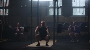 Three fitness man bodybuilder training using barbell weightlifting exercise muscular sportsman power lifting heavy weight doing squats in gym practice enjoying healthy lifestyle.
