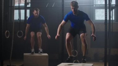 Multi-ethnic group of friends jumping onto wooden boxes in a crossfit training. Slow motion
