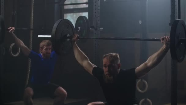 Two athlete lifts the bar above himself, performing a jerk, a spinning push. 2 man with a beard is engaged in weightlifting on a dark background, portrait. Concept strength, power, playing sports. — Stok video