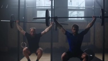 Two athlete lifts the bar above himself, performing a jerk, a spinning push. 2 man with a beard is engaged in weightlifting on a dark background, portrait. Concept strength, power, playing sports. 