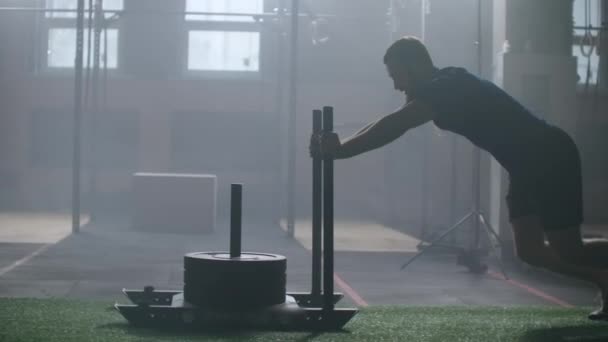 Joven hombre atlético caucásico fuerte que hace ejercicio con el trineo de entrenamiento de peso pesado hacia la cámara en el gimnasio grande cámara lenta — Vídeo de stock