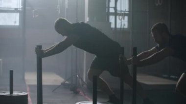 Motivation concept,two young athletic blonde man pushing heavy training sled towards camera training in gym slow motion