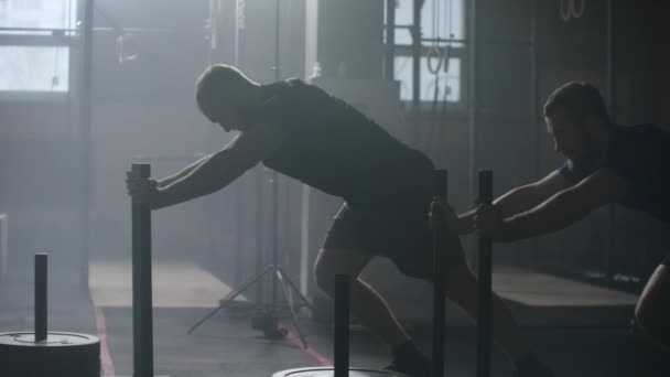 Концепция мотивации, два молодых спортсмена-блондина, толкающие тяжелые санки к тренировкам камеры в спортзале замедленной съемки — стоковое видео