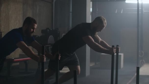 Dos jóvenes fuerte atlético caucásico hombre haciendo ejercicio con peso pesado trineo de entrenamiento hacia la cámara en gran gimnasio cámara lenta . — Vídeos de Stock