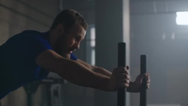 Willpower en motivatie, camera volgt jonge atletische man duwen zware training slee training in de sportschool slow motion — Stockvideo