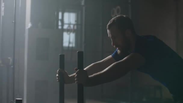 Siła woli i motywacja, kamera śledzi młodego sportowca pchającego ciężki trening sanek w siłowni slow motion — Wideo stockowe