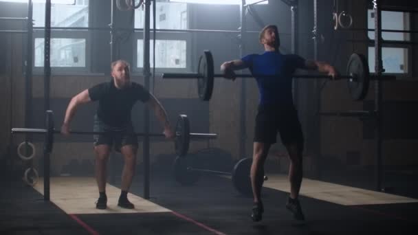 Two strong athletic people squat with a raised barbell over their head in slow motion. — Stockvideo