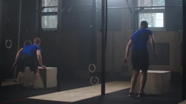 Ajuste atlético dos hombres hace saltos de caja en el gimnasio de la fábrica desierta. El ejercicio intenso es parte de su programa diario de entrenamiento físico cruzado. cámara lenta — Vídeos de Stock