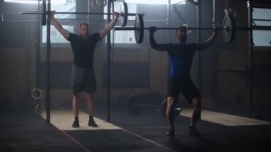 Two strong man doing weightlifting training together at the gym. Medium shot slow motion pan men exercising in gym with exercise equipments: Overhead squats, plate lunges, medicine ball, olympic rings