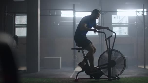 Slow motion Fit young man using exercise bike at the gym. Fitness male using air bike for cardio workout at cross training gym — 비디오