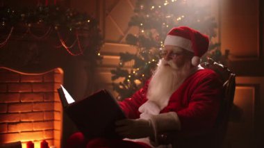 Santa Clauss magic room sits in a beam of light at home against the background of a fireplace and a Christmas tree on Christmas eve