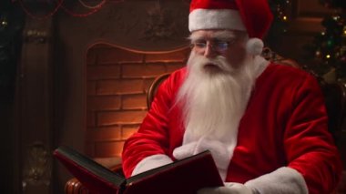 Old Santa Claus with a beard reading a book on the background of a Christmas tree