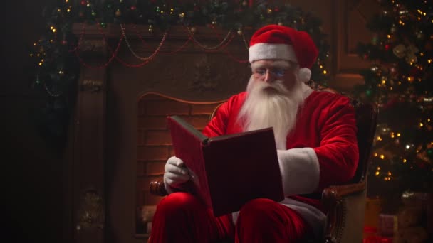Papai Noel trabalha na véspera de Natal lendo um livro em uma cadeira — Vídeo de Stock