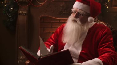Real Santa Claus reading a book at home by the fireplace