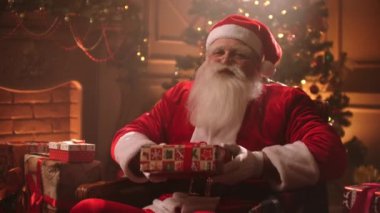 In a magical atmosphere on Christmas eve, Santa hands a gift to the camera with a smile.