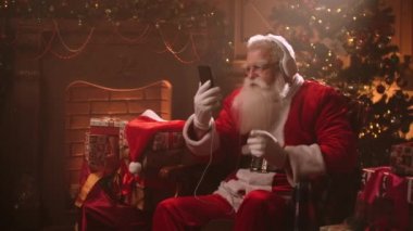 Dancing Santa Claus with headphones and a mobile phone in his hands. Listen to music online. Jerky and dynamic songs