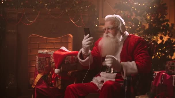 Dançando Papai Noel com fones de ouvido e um celular em suas mãos. Ouça música online. Músicas vibrantes e dinâmicas — Vídeo de Stock