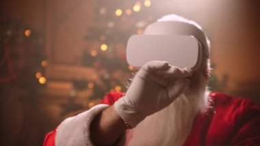 A modern Santa Claus sits in a chair and uses virtual reality technology to buy and send gifts to children