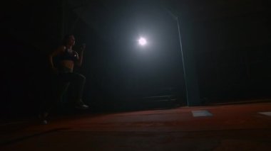 A sporty woman runs up in a stadium and performs a long jump in slow motion in a stadium on a dark background