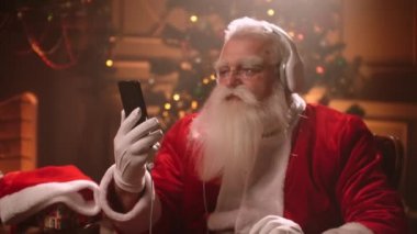 Santa Claus is having fun and relaxing listening to Christmas music in headphones