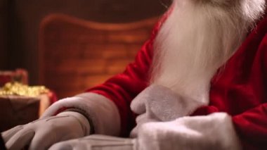 Santa Claus is working with a laptop looking through mail and answering messages to children. Choosing and ordering online gifts for children for Christmas.